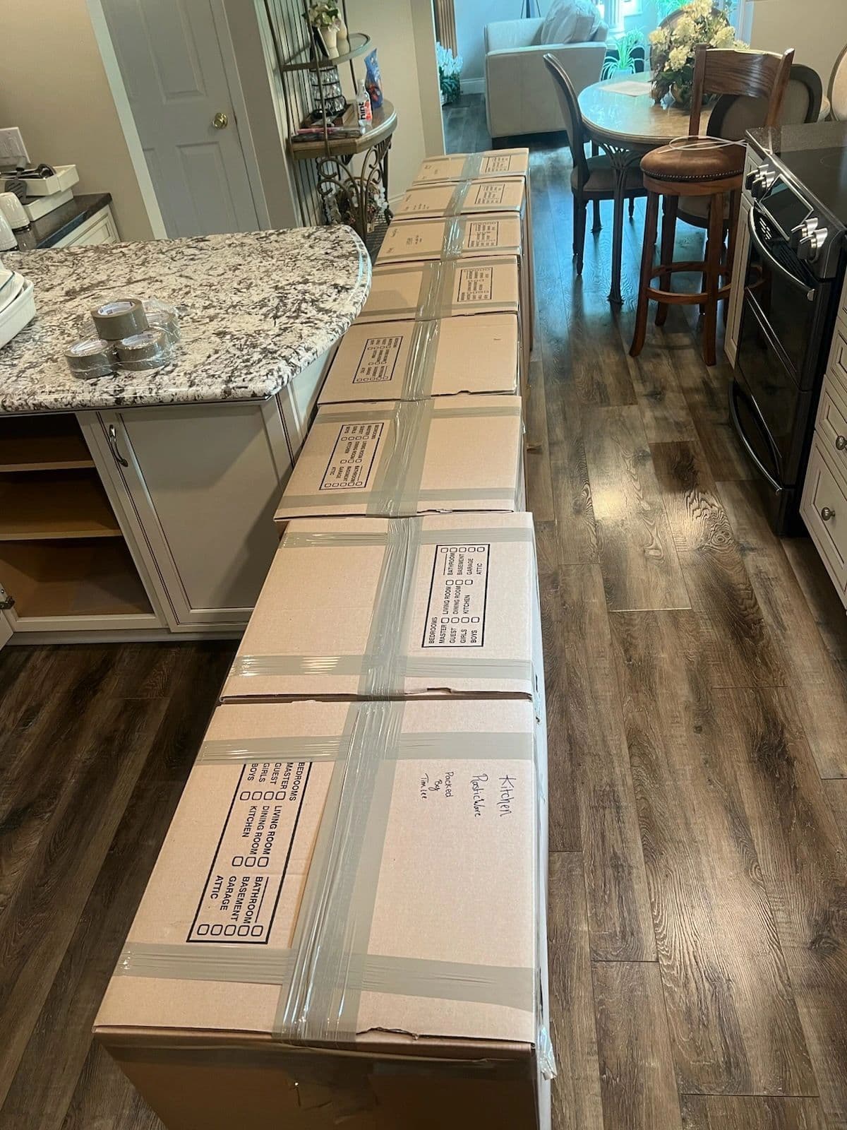 A row of packed, taped, and room-labeled moving boxes lined up through the kitchen